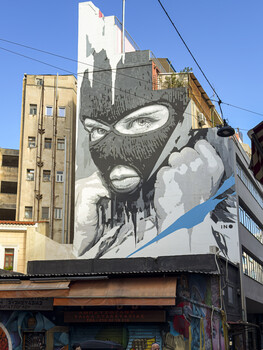 A mural of a masked person on a building in Athens, Greece.