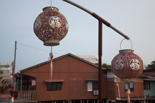 Two ornate spherical lanterns with filigree patterns suspended from a metal frame structure above traditional Asian architecture