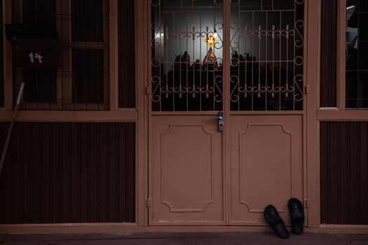 Pair of black shoes sitting against a terracotta-colored wooden door with ornate panels and decorative ironwork