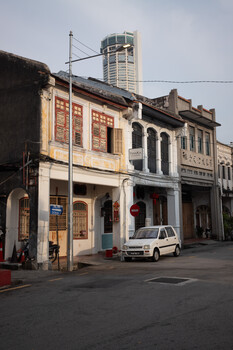 Row of weathered shophouses with faded signage and a modern high-rise building in the background
