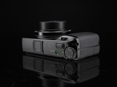 Compact rangefinder camera with attached lens viewed from above against black background