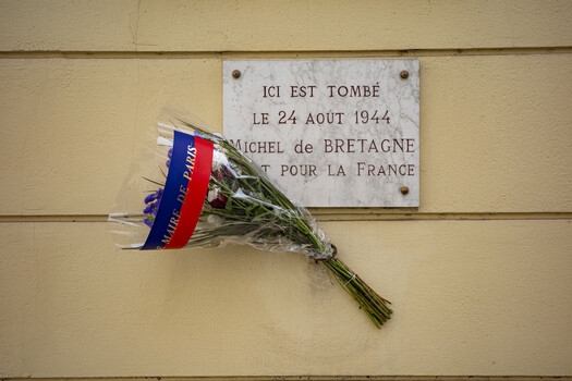 Memorial plaque with fresh flowers tied in French flag ribbon against cream-colored wall