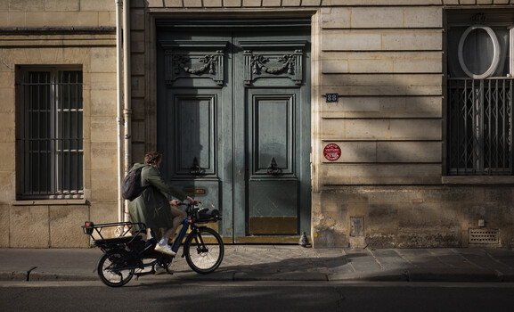 Person on electric cargo bike stopped in front of ornate dark green doors on Parisian street
