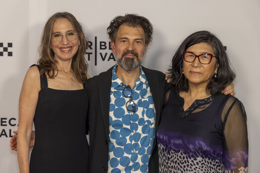 Three people posing together at a media event with festival branding visible in background