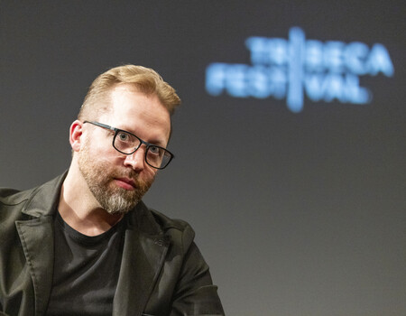 Man with glasses and beard wearing dark blazer at speaking event
