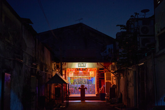 Narrow alleyway at dusk with warm neon signage illuminating traditional storefront