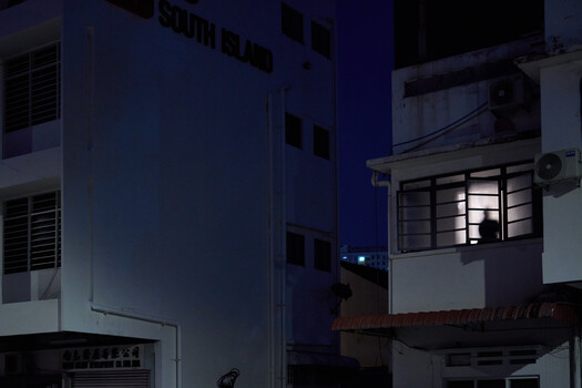 Nighttime urban street scene with multi-story residential buildings lit by artificial light
