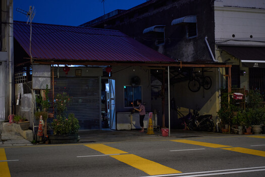 Nighttime storefront with blue metal shutter door and purple roof beneath highway overpass