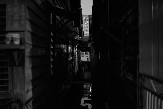 Narrow urban alleyway shot in high-contrast black and white, with wet pavement reflecting light