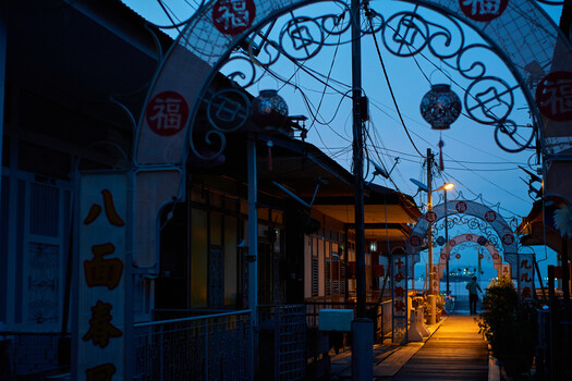 Twilight street scene with ornate blue archway and warm-lit storefronts in Asian urban setting