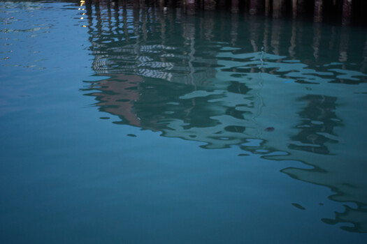 Reflections of wooden pier pilings in calm blue-green water