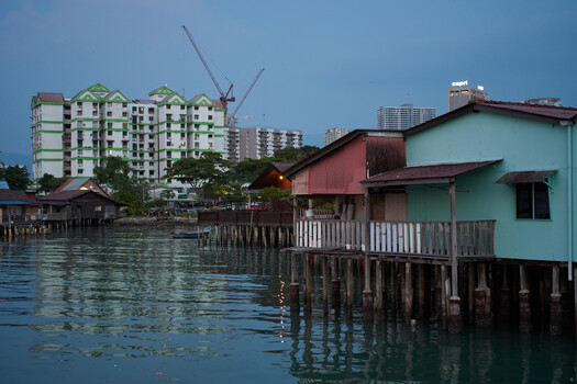 Waterfront stilt houses with modern apartment buildings beyond in blue twilight