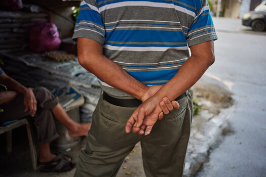 Man in blue and gray striped shirt standing outdoors with hands clasped at waist