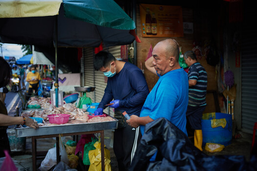 Street vendor preparing food at outdoor market stall under teal umbrellas