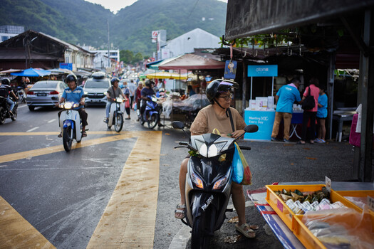 Motorcyclist in brown shirt riding black scooter on crowded street market