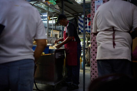 Street vendor serving food at a busy night market stall surrounded by customers