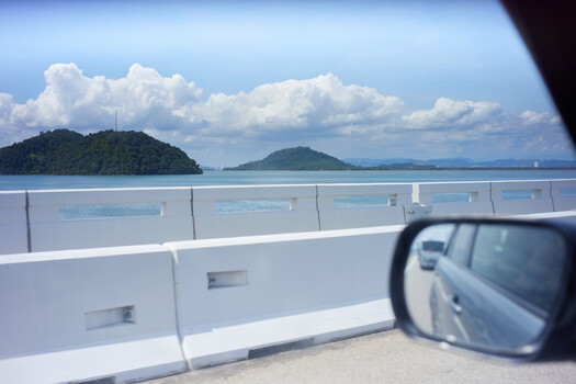 View from a ferry railing toward forested islands and calm turquoise water under partly cloudy sky