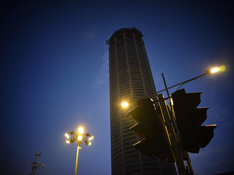 Tall residential tower illuminated at dusk with traffic light and street lamp in foreground