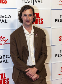 Man in brown blazer and white shirt at festival event backdrop
