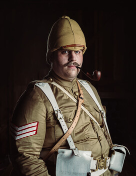 Portrait of man in vintage military uniform with peaked cap and pipe against dark background