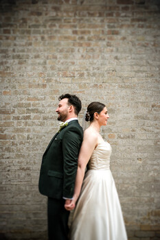 Bride and groom standing back-to-back against weathered brick wall
