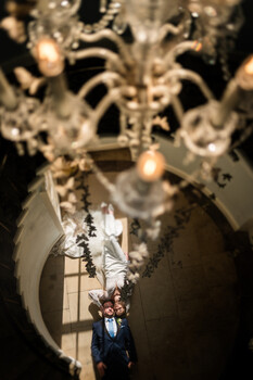 Man in suit standing beneath ornate white architectural ceiling with dramatic overhead lighting