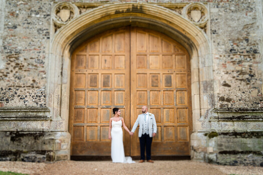 Bride and groom holding hands standing before large wooden arched doors
