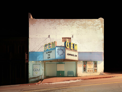 Abandoned vintage movie theater with faded signage photographed at night against dark sky