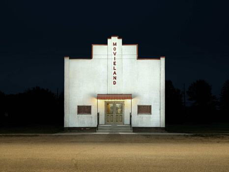 Illuminated white Art Deco movie theater facade with vertical neon sign reading "MOVIELAND" against dark night sky