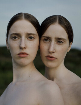 Two young women with dark hair positioned side-by-side against a soft, blurred natural background