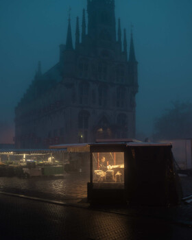 Illuminated glass booth in foreground with Gothic cathedral silhouetted in misty background