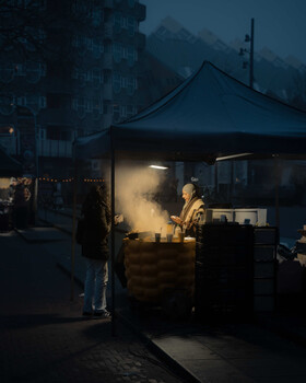 Person standing beside a glowing food stall in blue twilight urban setting