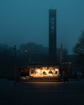 Illuminated storefront glowing against dark twilight sky with tall cylindrical tower structure