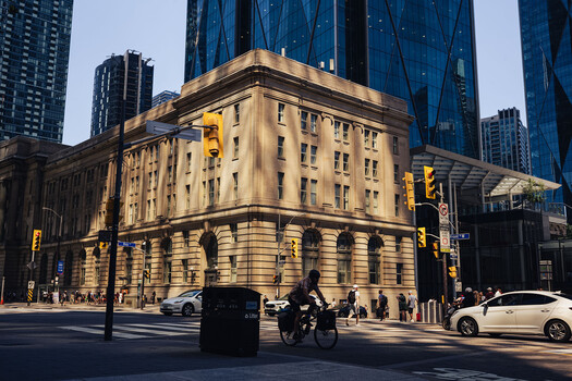 Neoclassical stone building with modern glass skyscrapers rising behind it on urban street