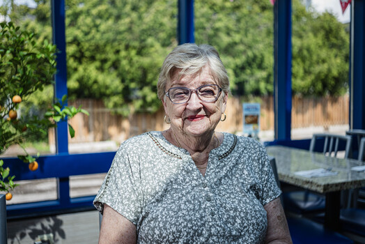 Older woman with gray hair and glasses smiling at camera outdoors
