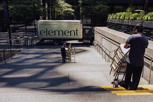 Urban outdoor scene with Element food truck and workers arranging metal chairs