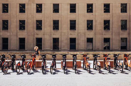 Row of orange and yellow bikes lined up against a tan building facade with grid of dark windows