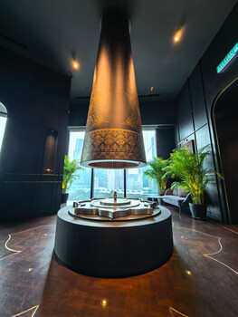 Large illuminated cone-shaped pendant light suspended above a circular display platform in a modern interior gallery space