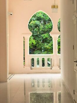 Minimalist architectural hallway with arched Moorish window framing lush green foliage
