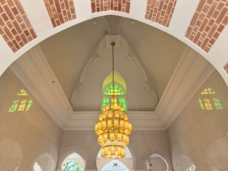 Interior of a chapel with ornate golden chandelier centered under a vaulted ceiling with colorful stained glass windows