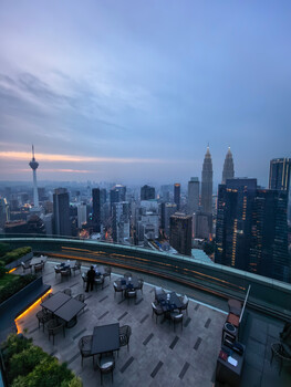 Kuala Lumpur skyline at dusk from a rooftop observation deck with Petronas Twin Towers prominent