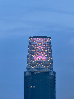 Modern skyscraper tower top with illuminated geometric lattice pattern against twilight sky