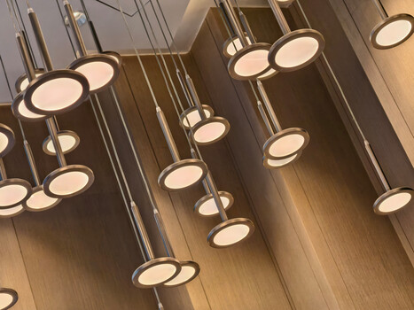Multiple pendant lights with circular diffusers suspended at varying heights against wooden ceiling
