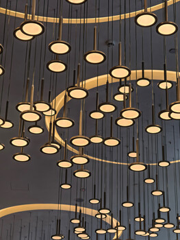 Modern chandelier with multiple circular brass pendant lights suspended at varying heights against dark ceiling