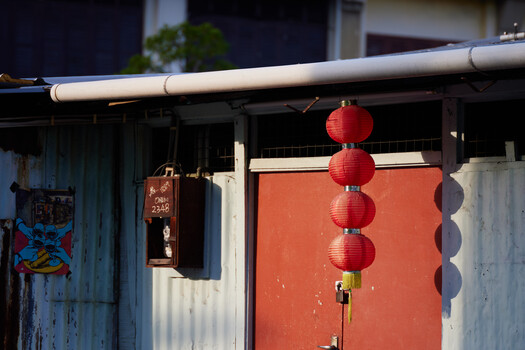 Red paper lanterns hanging from a bamboo pole above an orange corrugated metal door