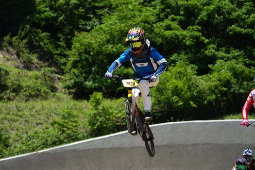 BMX rider airborne on concrete track with green hillside backdrop