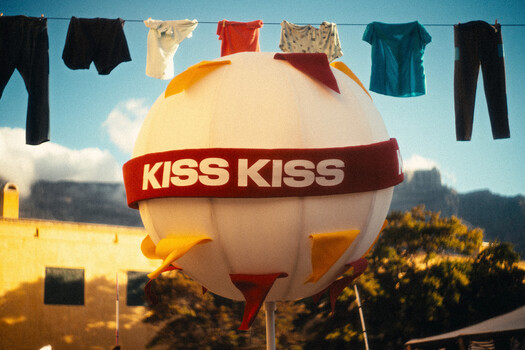 Large white hot air balloon with red "KISS KISS" band against blue sky, clothesline with hanging garments above
