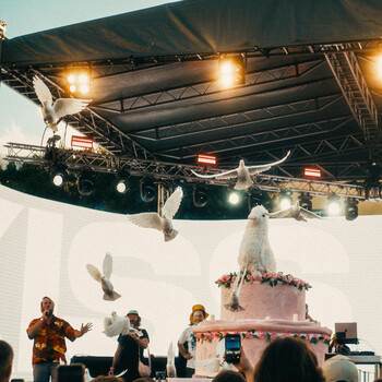 Event stage setup with pink tiered cake and decorative white backdrop under professional stage lighting