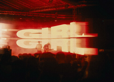 Silhouetted crowd watching large red-lit stage display with glowing text