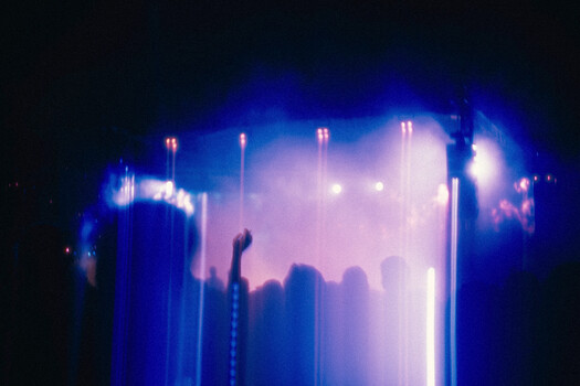 Concert crowd silhouetted against bright stage lighting with blue and pink color cast